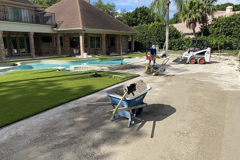 Artificial turf being installed across the same pool backyard