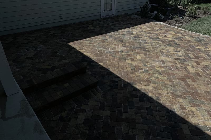 Brick paver patio in warm red and tan tones, laid in a herringbone pattern