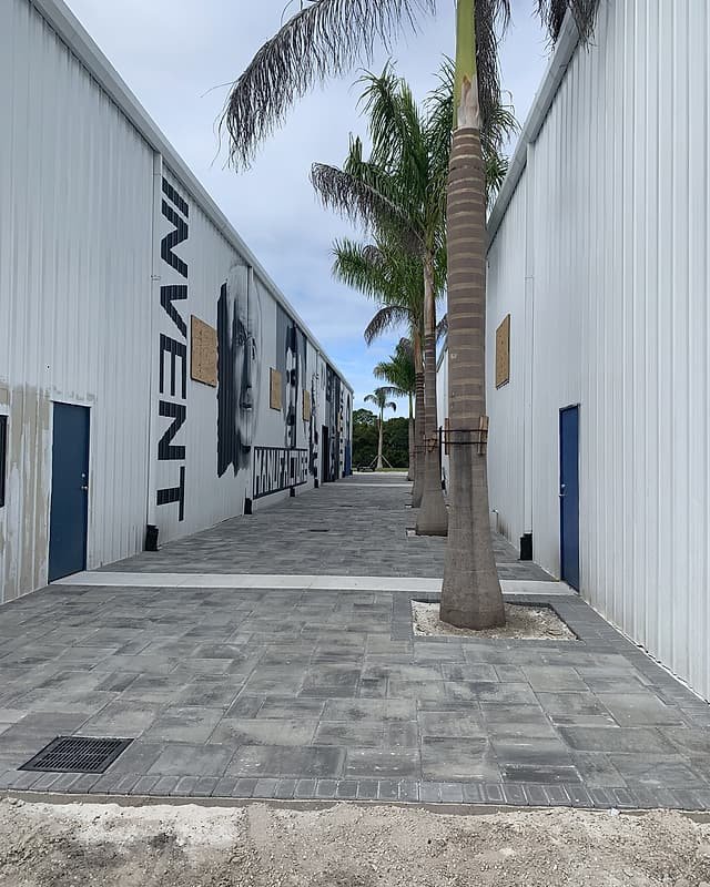 Paver alley between commercial buildings with palm trees and a drain grate