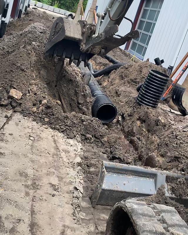 Excavator trench with corrugated drain pipe and a catch basin ready for installation