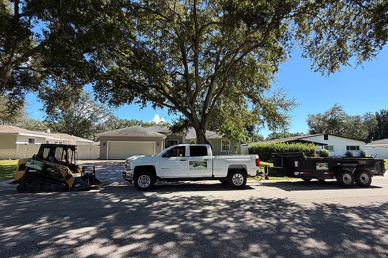 Track loader, work truck and dump trailer lined up on a residential street