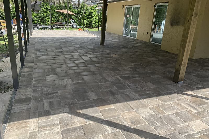 Covered lanai paved with gray blend pavers, opening onto the backyard