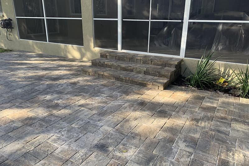 Paver patio meeting steps up to a screened porch, with fresh planting along the edge