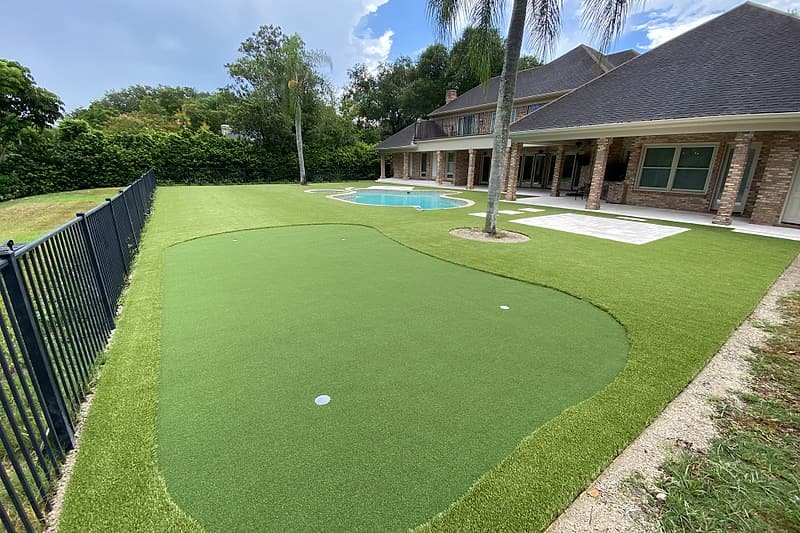 Backyard putting green with a cup, set into an artificial turf lawn beside a pool