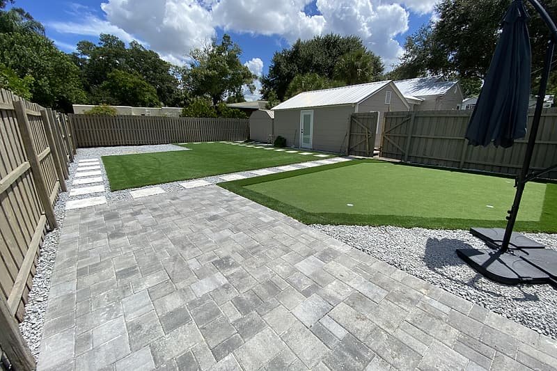 Paver patio leading to a lawn with a lighter putting green area