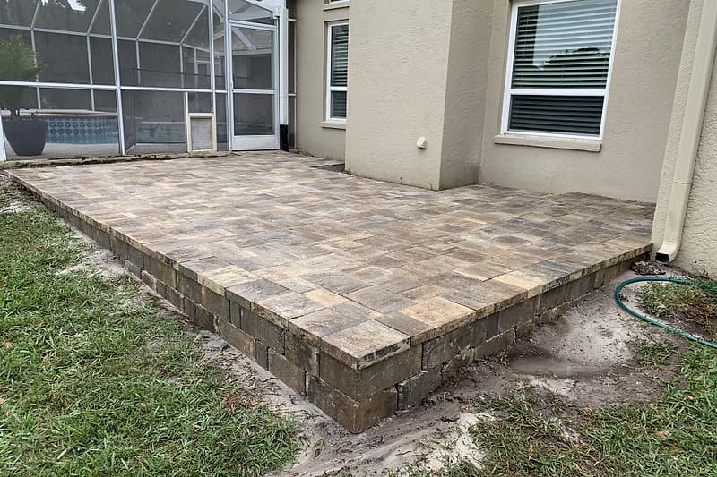 Raised paver patio with a block border beside a screened pool enclosure