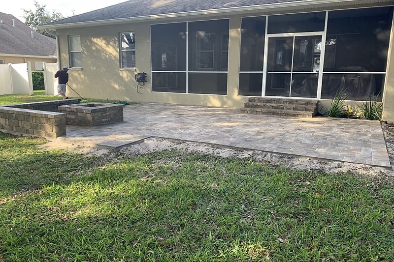 Backyard paver patio with a fire pit and block seating walls in front of a screened porch