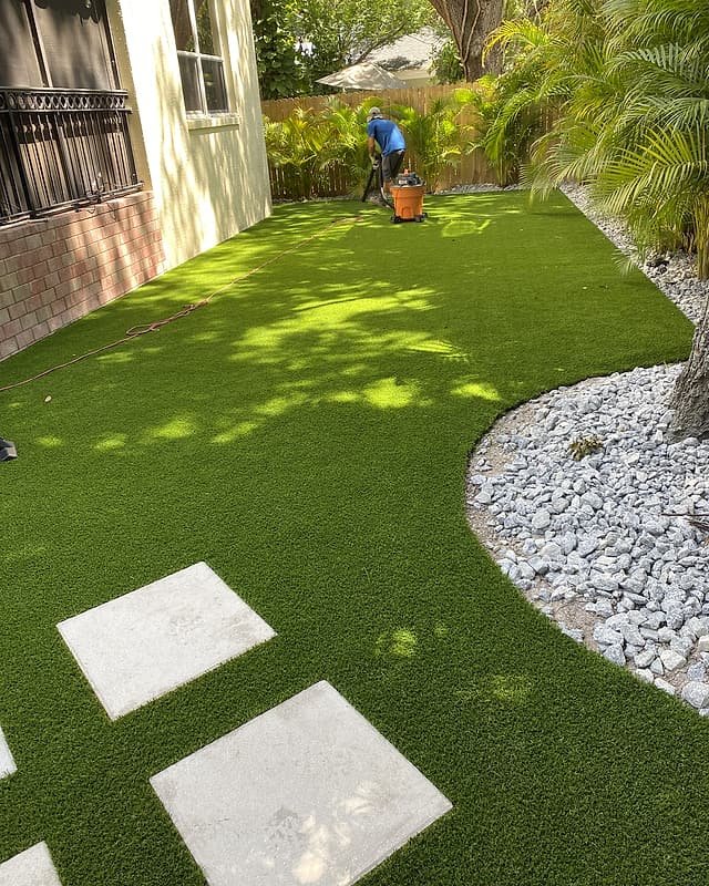 Curved edge of artificial turf meeting a white rock bed, with large square pavers