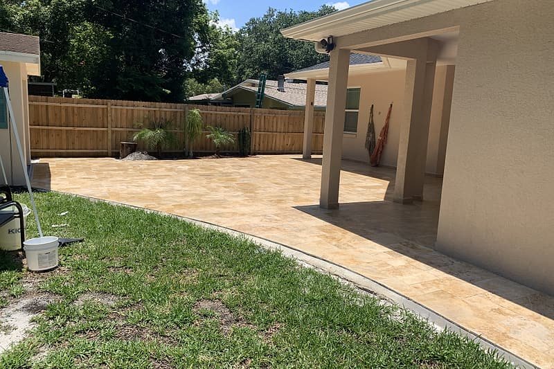 Travertine patio curving around a covered porch, edged by lawn