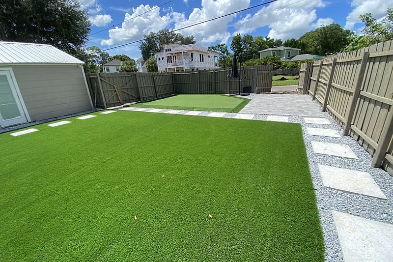 Rectangular artificial turf lawn edged with gravel and a path of square pavers