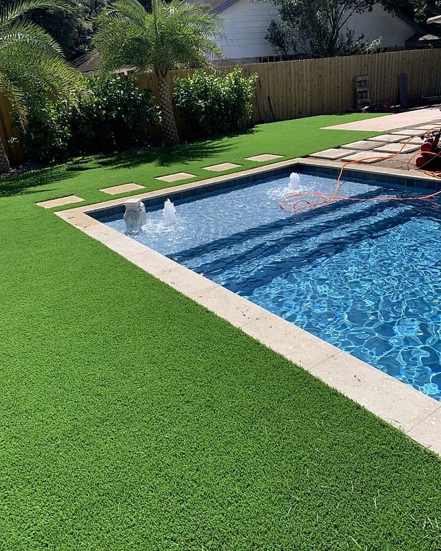 Artificial turf framing a rectangular pool, with square stepping pads set into the lawn
