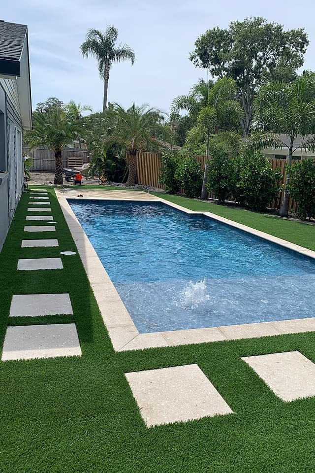 Narrow side lawn of artificial turf with stepping pads running beside a pool