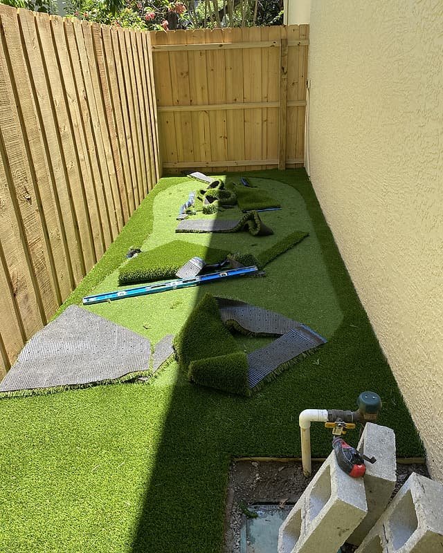Artificial turf being rolled out and trimmed in a narrow side yard