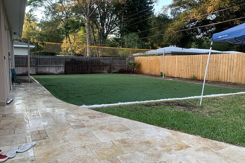 Backyard of artificial turf bordered by a travertine patio and walkway